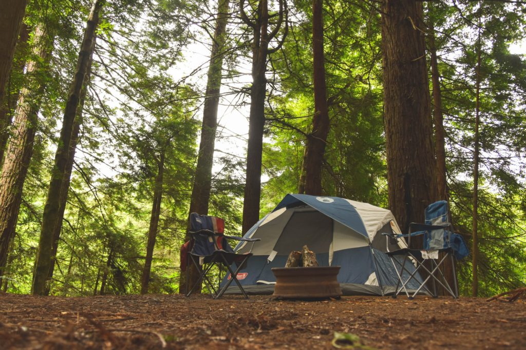 camping in woods with tent and two camp chairs