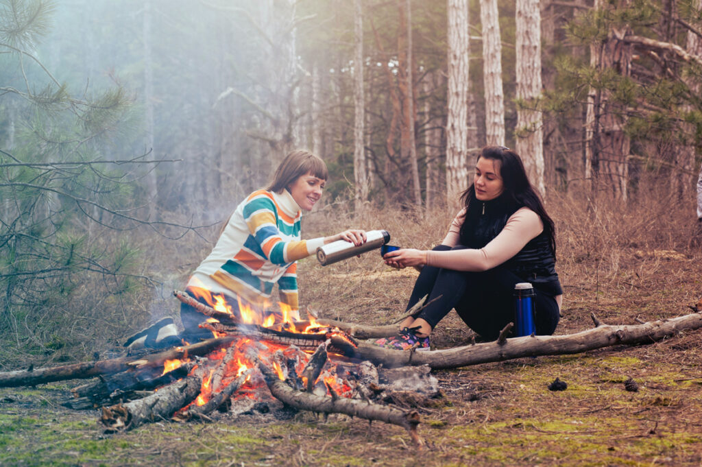 Sharing cups of warm drink beside a campfire